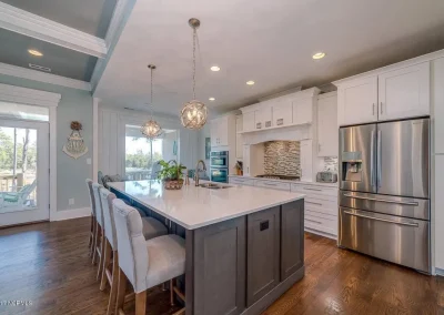Modern kitchen with white cabinets, stainless steel appliances, and a large island with four upholstered chairs.