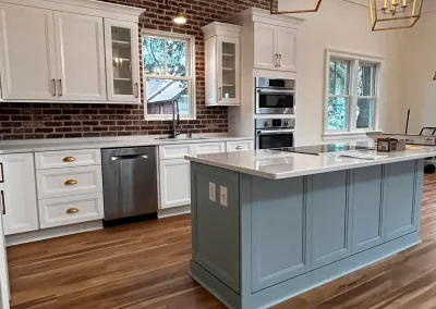 Modern kitchen with brick backsplash, white cabinets, blue island, wood floors, and gold pendant lights.