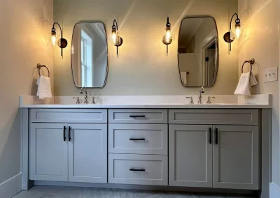 Modern bathroom with dual sinks, oval mirrors, wall sconces, gray cabinets, and marble tile flooring.