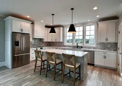 Modern kitchen with white cabinets, island, three chairs, pendant lights, and stainless steel appliances.
