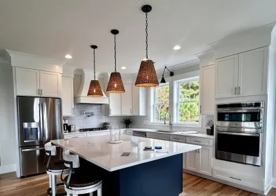 Modern kitchen with white cabinets, a navy island, pendant lights, stainless appliances, and wood floors.