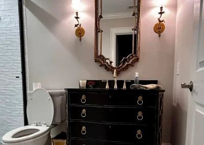 Elegant bathroom with a black vanity, ornate mirror, toilet, and wall sconces on either side of the mirror.