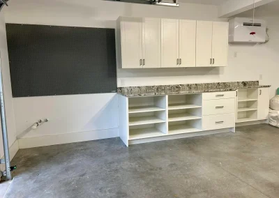 Garage with white cabinets, granite countertop, pegboard, and exposed concrete floor.