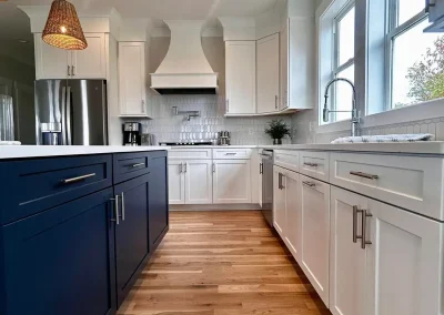 Modern kitchen with blue island cabinets, white cabinetry, wood floor, and natural light from large windows.