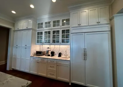 Modern kitchen with white cabinets, glass doors, built-in fridge, appliances, and under-cabinet lighting.