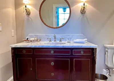 Elegant bathroom with a wood vanity, round mirror, marble countertop, and wall sconces.