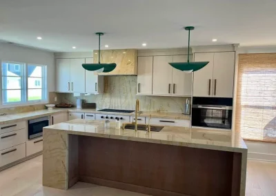 Modern kitchen with white cabinets, marble countertops, green pendant lights, and large windows.