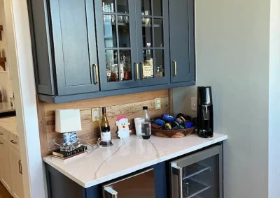 A small home bar with glass cabinets, wine fridge, coffee machine, and fruit decor on top.
