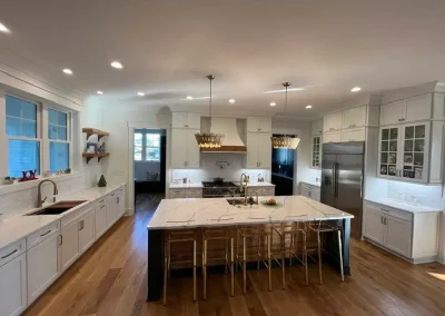 Spacious modern kitchen with white cabinets, marble island, wooden floor, and pendant lights.