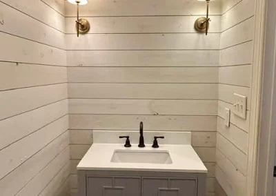 Small bathroom with shiplap walls, a gray vanity, two wall sconces, and wood flooring.