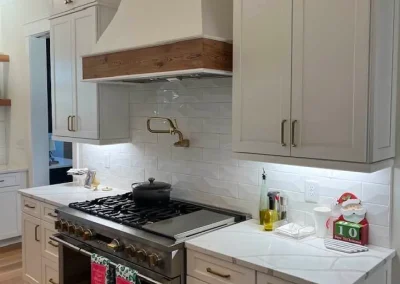 Modern kitchen with white cabinets, a gas stove, range hood, and holiday-themed towels hanging on the oven.