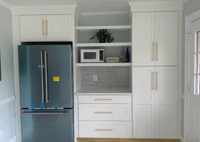 Modern kitchen with white cabinets, a stainless fridge, microwave, shelves, and a striped rug on tiled floor.