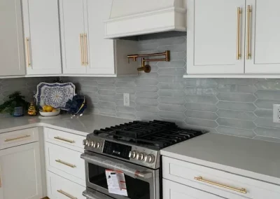 Modern kitchen with white cabinets, gold handles, gray backsplash, and a stainless steel gas stove.