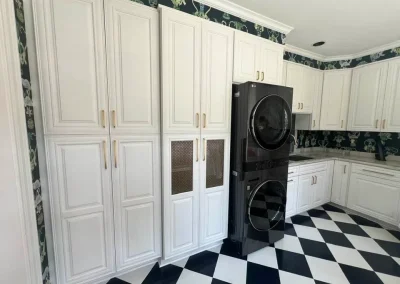 White kitchen with black and white checkered floor, stacked black washer and dryer, and floral wallpaper.