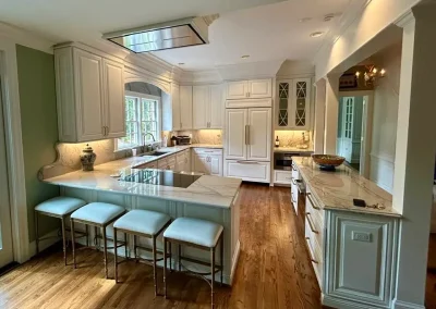 Spacious kitchen with white cabinets, marble countertops, island seating, and wooden floors.