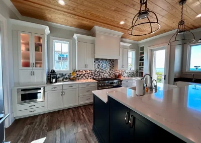 Modern kitchen with white cabinets, large island, wood ceiling, and patterned backsplash, sunlight streaming in.