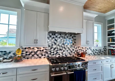 Modern kitchen with white cabinets, stainless steel stove, tiled backsplash, wood ceiling, and windows.