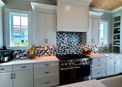 Modern kitchen with white cabinets, marble island, and a black-and-white tiled backsplash behind the stove.