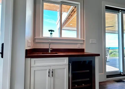 Small kitchenette with white cabinets, dark wood counter, a sink, window, and glass-front mini fridge.