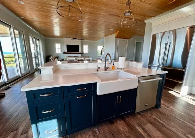 Modern kitchen with navy cabinets, farmhouse sink, and stainless appliances, open to a bright living area.