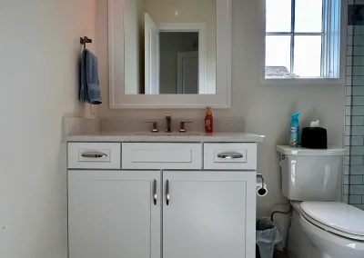 Modern bathroom with a white vanity, mirror, toilet, towel, soap, and window letting in natural light.