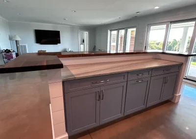 Modern kitchen island with gray cabinets, marble countertop, and a raised dark wood bar in a bright open room.