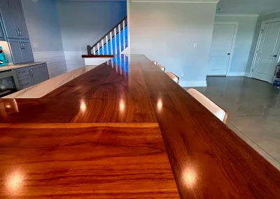 A polished wooden kitchen island with chairs, facing a staircase and doors in a modern open space.