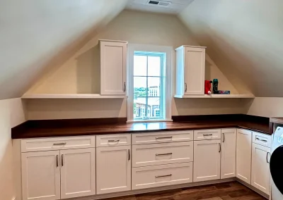 Room with sloped ceiling, white cabinets, wood countertop, and a window centered above the counter.