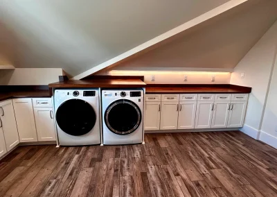 A laundry room with washer, dryer, white cabinets, wood counters, angled ceiling, and wood-look floor.