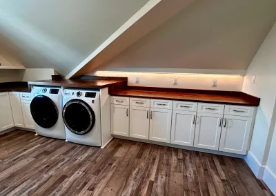 Laundry room with washer, dryer, white cabinets, wood countertops, and slanted ceiling.