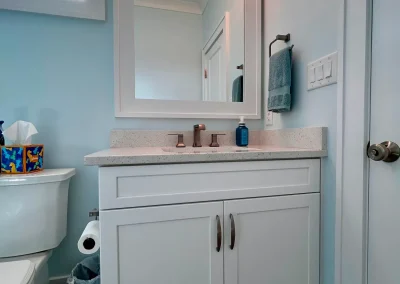 Modern bathroom vanity with a mirror, light, sink, and towel, next to a toilet and tissue box.