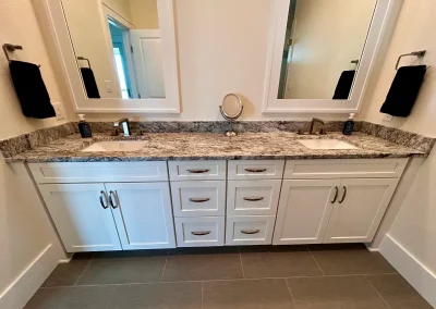 Double-sink bathroom vanity with granite countertop, two mirrors, white cabinets, and black hand towels.
