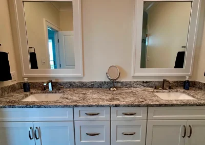 Double bathroom vanity with granite countertop, two sinks, two mirrors, white cabinets, and wall lights.