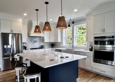 Modern kitchen with white cabinets, a navy island, pendant lights, and stainless steel appliances.