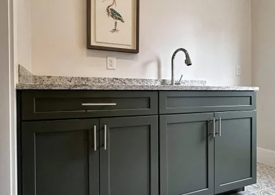 Dark green cabinets with a granite countertop, a sink, and a bird picture hanging above.
