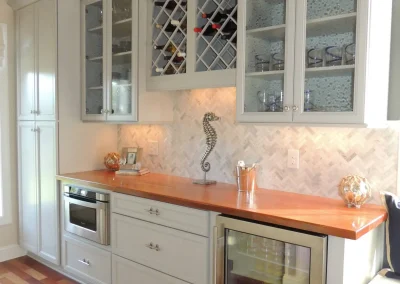 Modern kitchen nook with glass cabinets, wine rack, built-in fridge, microwave, and wooden countertop.