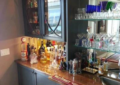 Home bar with liquor bottles, glassware, mirrored shelves, and a small sink on a wooden countertop.