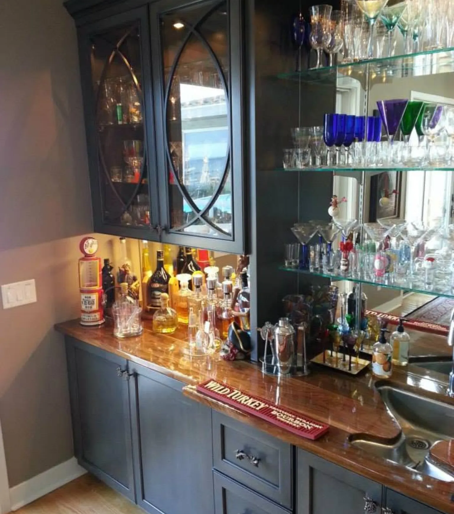 Home bar with liquor bottles, glassware, mirrored shelves, and a small sink on a wooden countertop.
