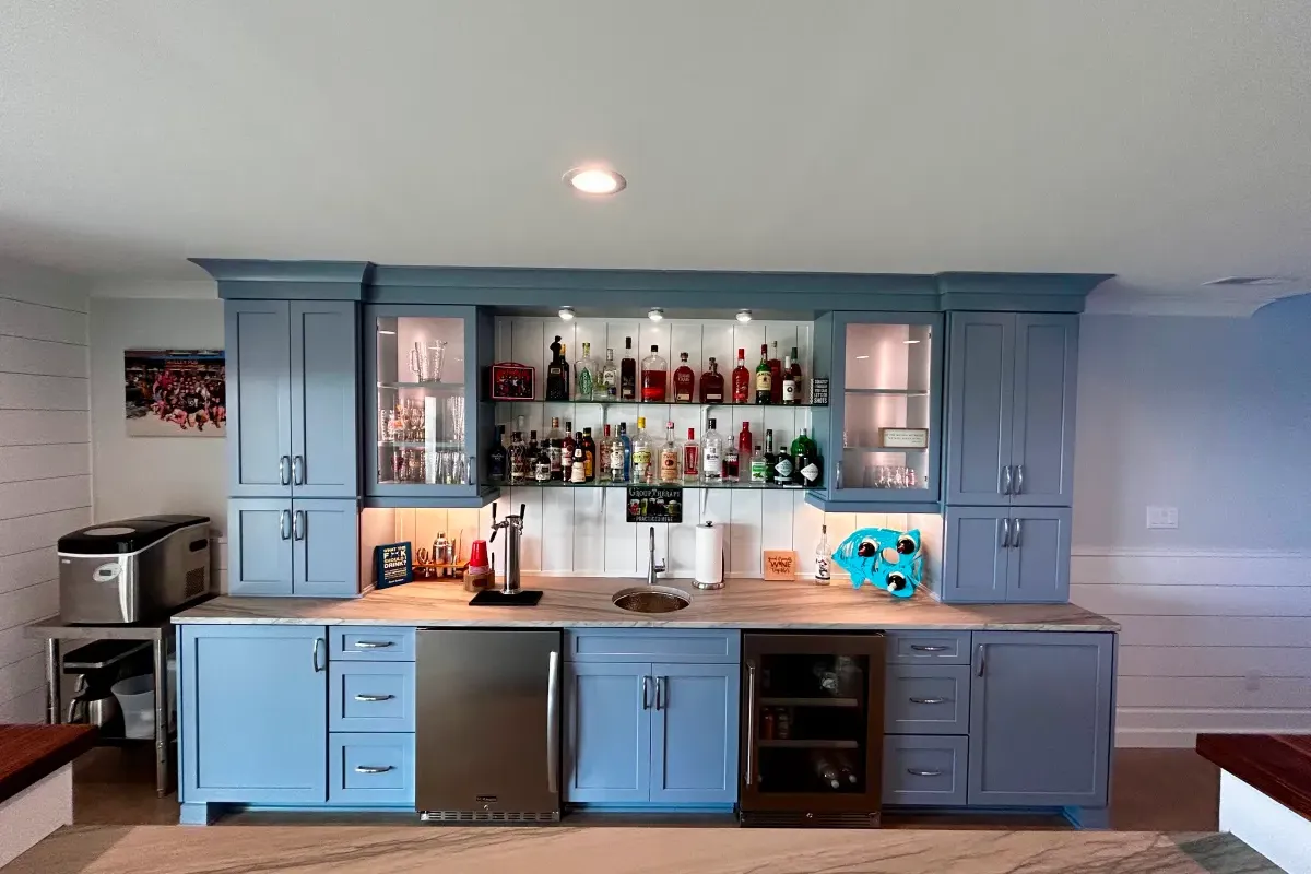 Home bar with blue cabinets, assorted bottles, glasses, mini fridge, and a margarita machine on the right.