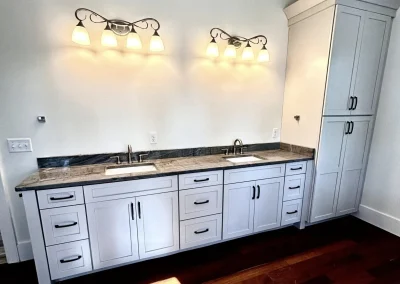 Double-sink vanity with white cabinets, marble countertop, tall cabinet, and two six-light fixtures above.