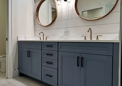 Blue double-sink vanity with marble countertop, gold faucets, and round mirrors above.