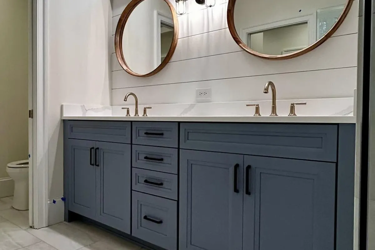 Blue double-sink vanity with marble countertop, gold faucets, and round mirrors above.