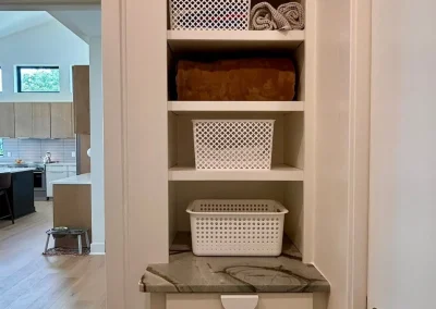 White shelves hold baskets and towels; a marble counter and drawers sit below in a hallway nook.