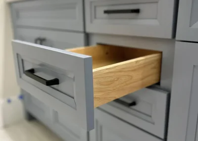 A gray bathroom vanity with one drawer open, revealing an empty wooden interior.