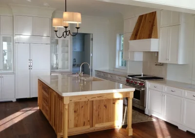 Bright kitchen with a large wooden island, white cabinets, stove, fridge, and pendant lights.