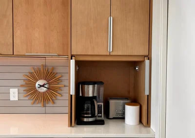 A coffee maker, toaster, and container sit in a small nook beneath wooden kitchen cabinets.