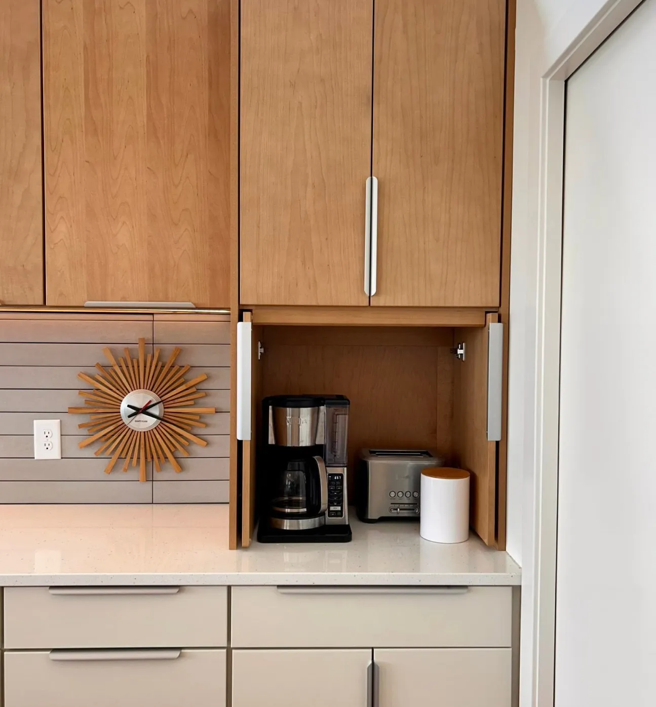 custom-1 A coffee maker, toaster, and container sit in a small nook beneath wooden kitchen cabinets.