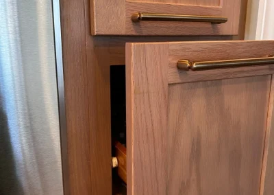 A narrow wooden pantry cabinet with the door slightly open, revealing shelves with kitchen items inside.