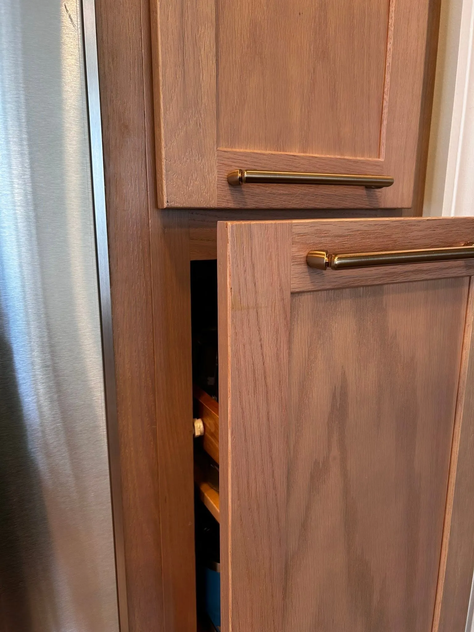 custom-2 A narrow wooden pantry cabinet with the door slightly open, revealing shelves with kitchen items inside.