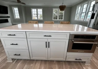 White kitchen island with drawers, cabinets, built-in microwave, and marble countertop in a bright room.